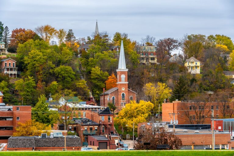 A historic brick cathedral surrounded by brick buildings, houses and fall leaves during Galena in the fall.