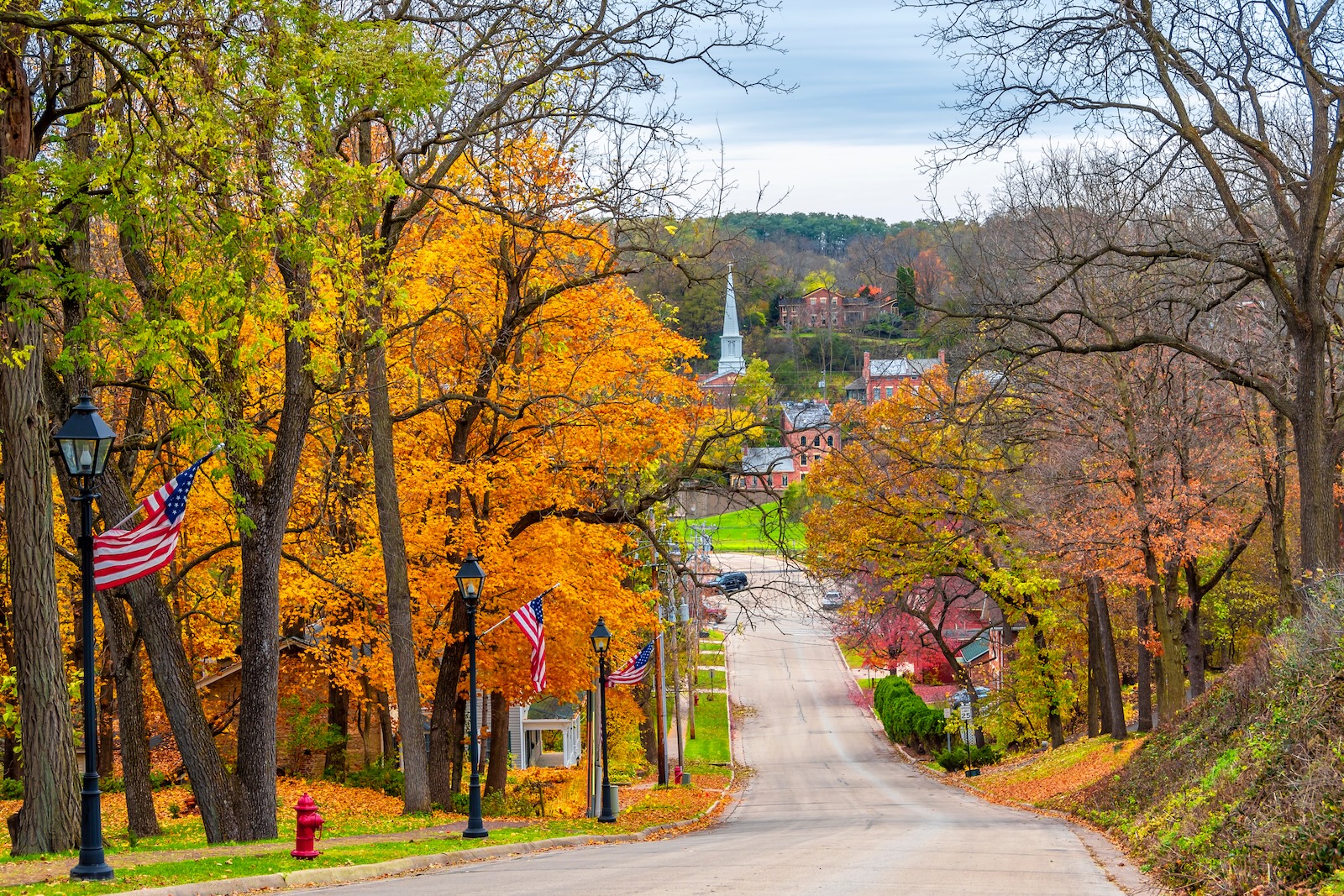 Galena in the Fall: A Complete Guide to Your Getaway 2 A historic road lined by orange, red, and yellow treas and American flags during Galena in the fall.