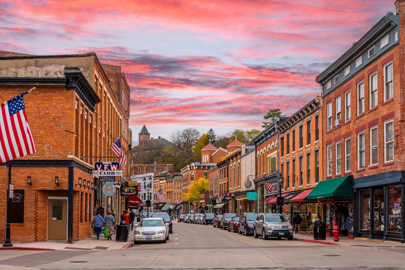 Galena in the Fall: A Complete Guide to Your Getaway 1 A downtown road lined by parked cars and historic brick buildings, with pops of fall foliage and a sunset, during Galena in the fall.