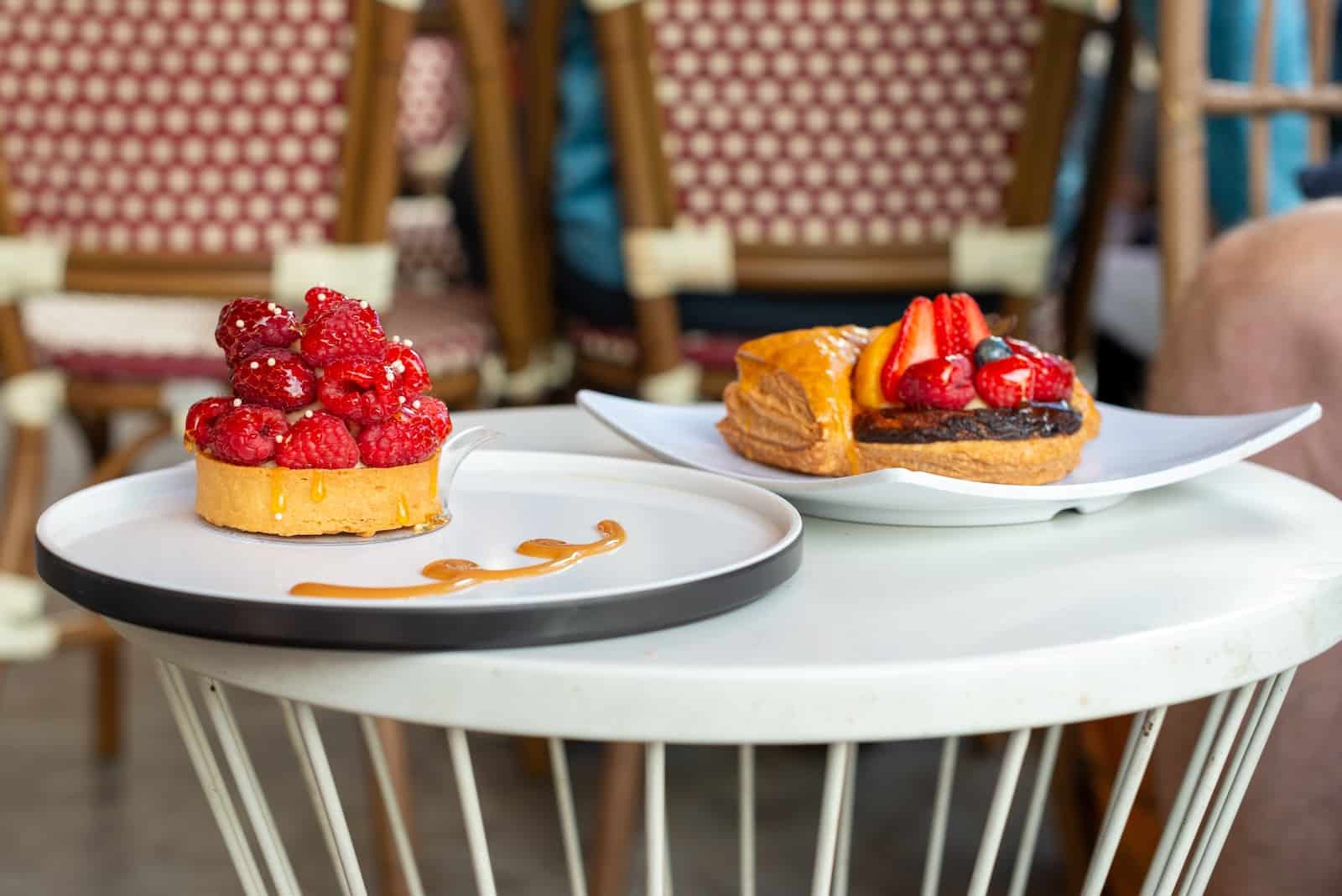 The Best Restaurants in Galena, IL: A Local's Guide 1 A fruit French puff pastry stuffed-custard tarte on a white square plate. The topping has fresh whole red raspberries, strawberries, and blueberries. The second plate has a raspberry tart with an almond crust on a round plate. The food is on a white round metal table at one of the best restaurants in Galena IL.